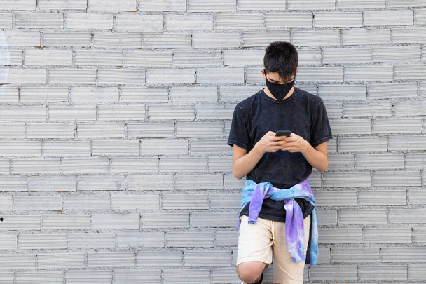 fiatal tinédzser egészségügyi maszk és mobiltelefon az utcai falon - Fotó, kép