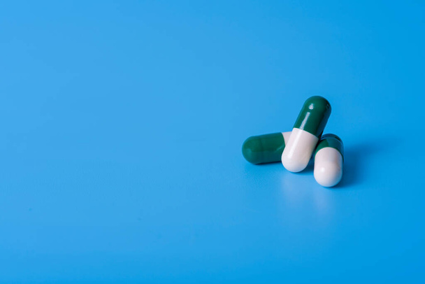 健康を維持するために青の背景に白い緑色のカプセル。健康と医療の概念. - 写真・画像