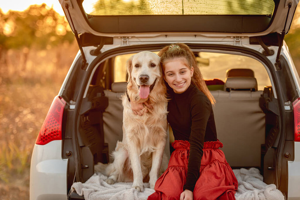 Adolescente chica abrazando perro en coche tronco - Foto, Imagen