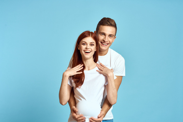 Mujer embarazada en camiseta blanca y hombre casado pareja esperando bebé azul fondo recortado vista de las emociones - Foto, imagen