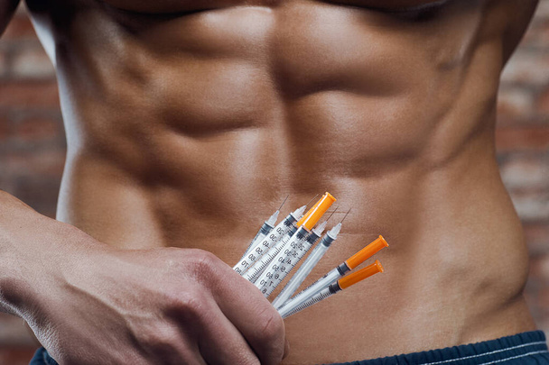 Bodybuilder doing steroid syringe injection in gym. Strong athletic rough muscular man pumping up abs muscles workout fitness and bodybuilding healthy concept design. abdominal exercises naked torso - Photo, Image