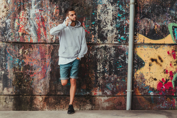 νεαρός άνδρας με κινητό τηλέφωνο στον τοίχο του δρόμου στην πόλη - Φωτογραφία, εικόνα