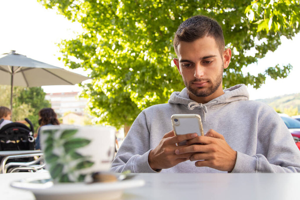 mladý muž v kavárně terasa s mobilním telefonem - Fotografie, Obrázek