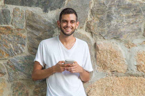 jonge man met mobiele telefoon op de muur buiten - Foto, afbeelding