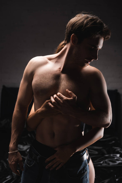Woman in panties hugging muscular boyfriend in bedroom during evening  - Foto, imagen