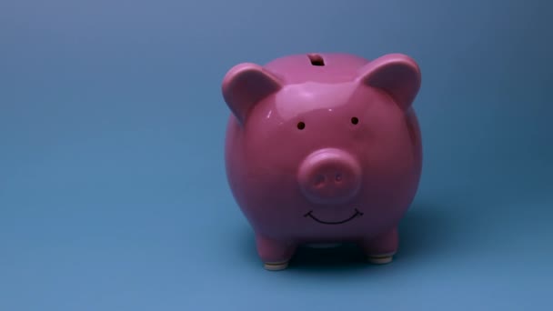 Finanzierungssparkonzept. Geld, das in das Sparschwein geworfen wird. Sparschwein wirft eine Kleinigkeit vor blauem Hintergrund. - Filmmaterial, Video