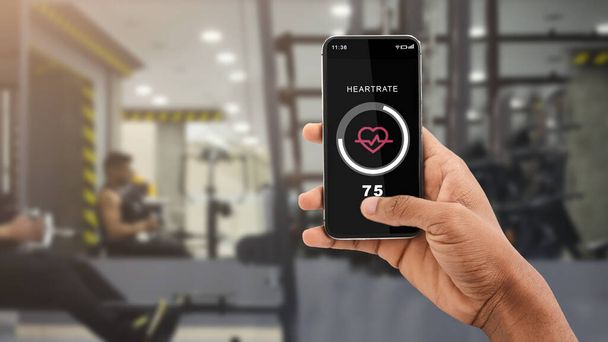 Modern workout with gadget and body care. African american male hand holds smartphone with heart rate - Photo, Image