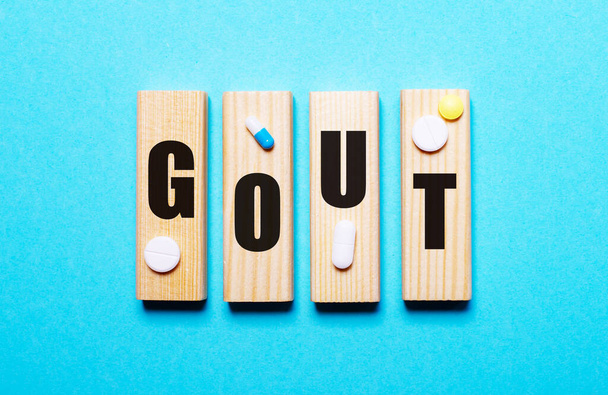 The word GOUT is written on wooden blocks on a blue background next to the pills. Medical concept - Photo, Image