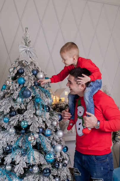 Happy Father and son enjoying decorating Christmas tree with Christmas balls and light garland preparing for celebrating winter holidays: Merry Christmas Eve and Happy New Year 2021. Family concept. - Foto, Bild