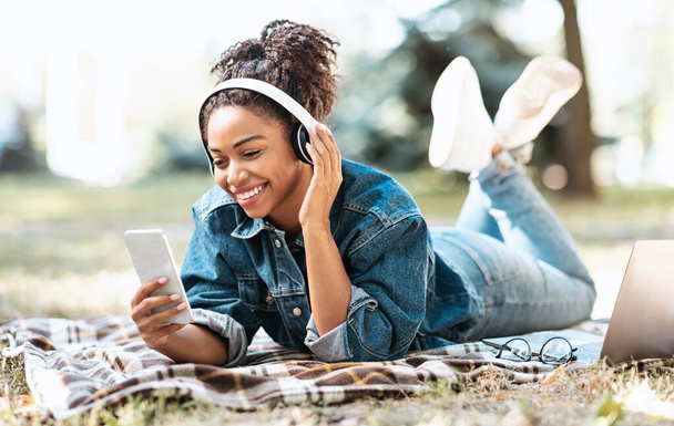 Zwarte dame met behulp van telefoon en koptelefoon Muziek Luisteren Liggen Buiten - Foto, afbeelding