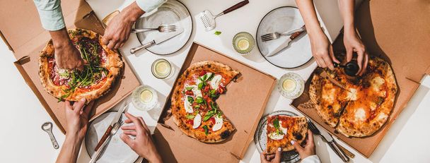 Pizza party for friends or family. Flat-lay of various pizzas, lemon drinks and peoples hands over white table background, top view. Fast food, comfort food, Italian cuisine concept - 写真・画像