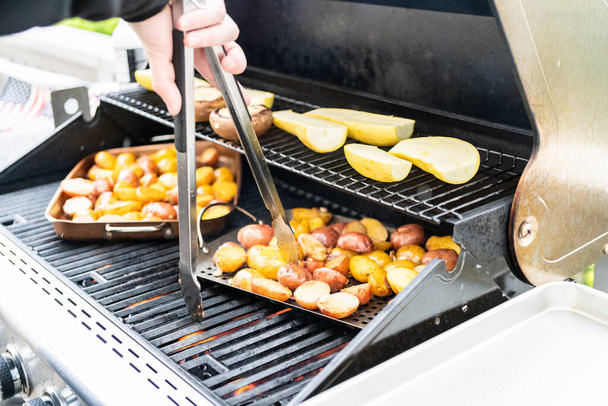 Grilling small potatoes with slices of garlic on an outdoor gas grill. - Photo, Image