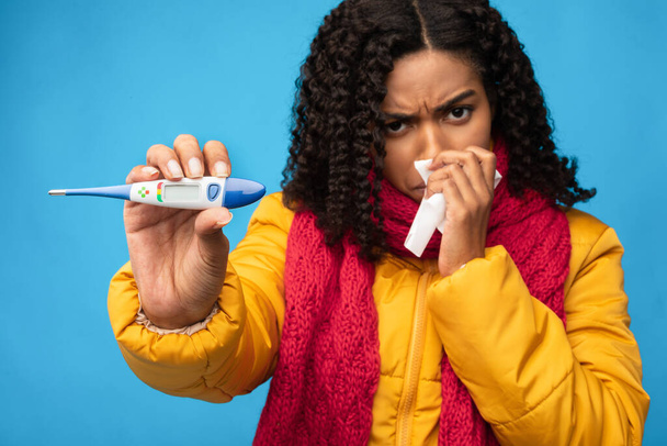 Mujer negra enferma mostrando termómetro teniendo fiebre sobre fondo azul - Foto, Imagen