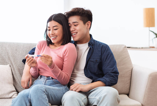 Joyful asiatisch pärchen holding positiv schwangerschaftstest sitting bei zuhause - Foto, Bild