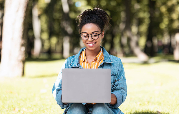 アフリカ系アメリカ人女子学生がノートパソコン学習を利用｜オンライン座り屋外 - 写真・画像