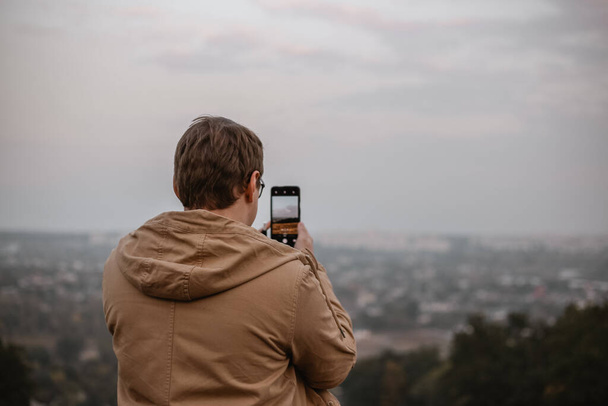 a man taking a photo of a landscape using his phone - Fotó, kép