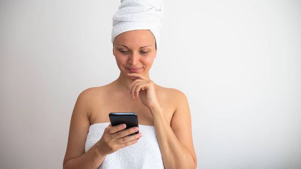 Donna dopo la doccia avvolto in un asciugamani navigazione sul telefono. - Foto, immagini