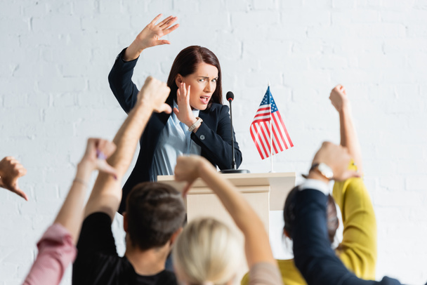 alto-falante chocado em pé na frente dos eleitores mostrando polegares para baixo na sala de conferências - Foto, Imagem