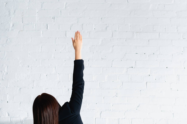 вид сзади женщины, голосующей рукой в воздухе о стену из белого брика - Фото, изображение