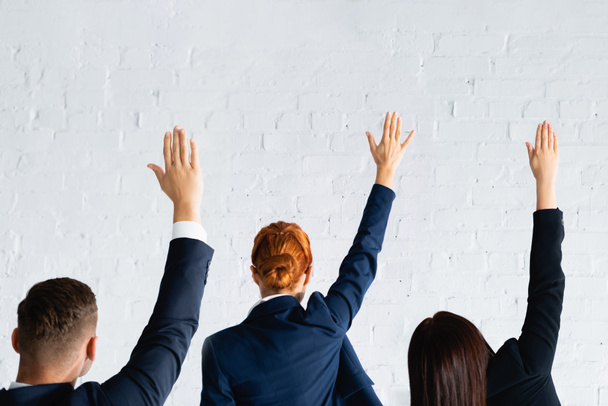achteraanzicht van vrouwen en mannen stemmen met handen in de lucht tegen witte bakstenen muur - Foto, afbeelding