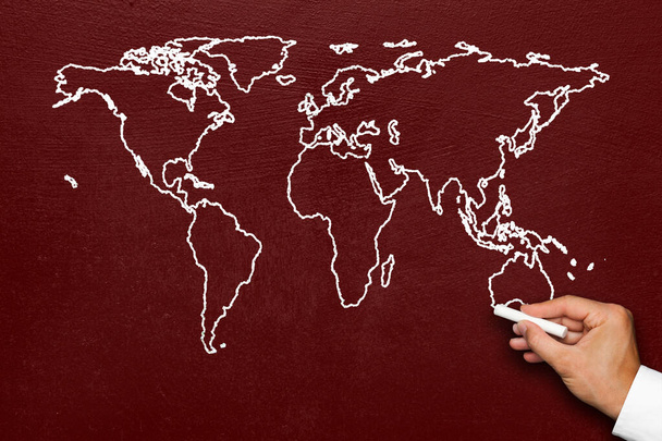 Mapa świata na tablicy. Ręka rysuje stylizowaną mapę świata globu z wszystkimi kontynentami z białą kredą na czerwonej tablicy. - Zdjęcie, obraz
