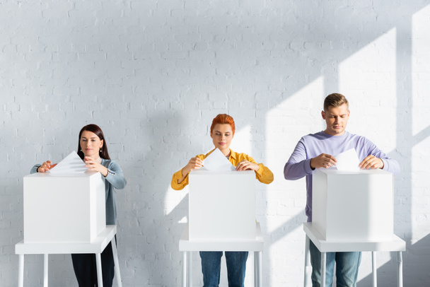 választópolgárok szavazólapokat helyeznek a szavazóurnákba a fehér téglafal ellen - Fotó, kép