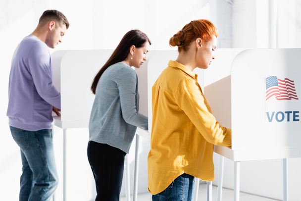 voliči ve volebních místnostech s americkou vlajkou a nápisy hlasování na rozmazaném pozadí - Fotografie, Obrázek