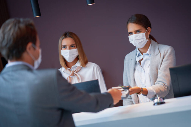 Businessman in mask at the reception of a hotel checking in - Foto, afbeelding