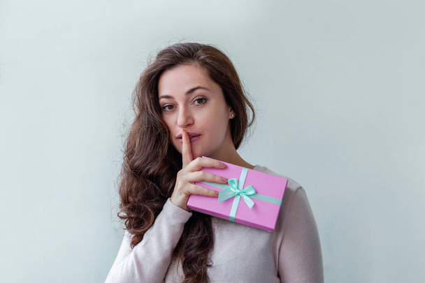 Young positive woman holding small pink gift box isolated on white background. Preparation for holiday. Girl looking happy and excited. Christmas birthday valentine celebration present concept - Фото, изображение