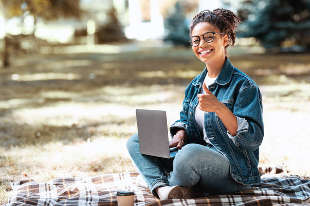 Afrikai nő laptoppal Gesztikuláló hüvelykujj fel ül a parkban - Fotó, kép