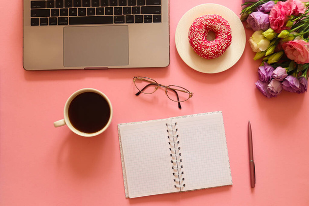 Business, freelance and education concept. Office desk with laptop, donut, coffee, notebook, glasses and flowers on pink background. Office desk working space. Top view, flat lay. - Фото, зображення