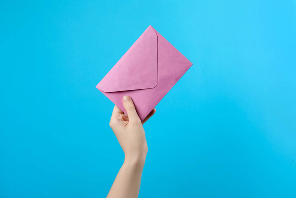 Woman holding pink paper envelope on light blue background, closeup - Foto, afbeelding