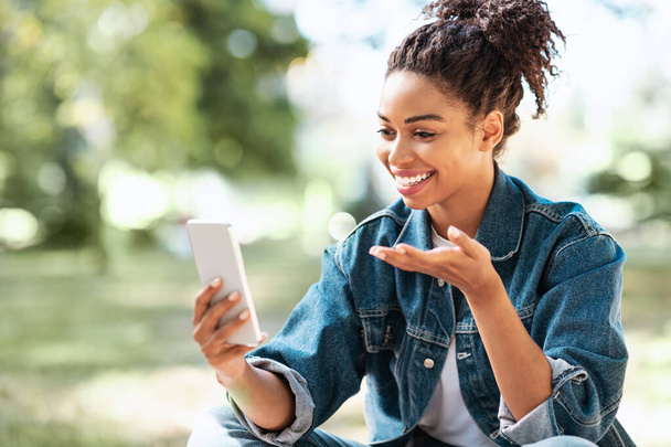 Alegre dama negra con teléfono haciendo videollamada sentado al aire libre - Foto, Imagen