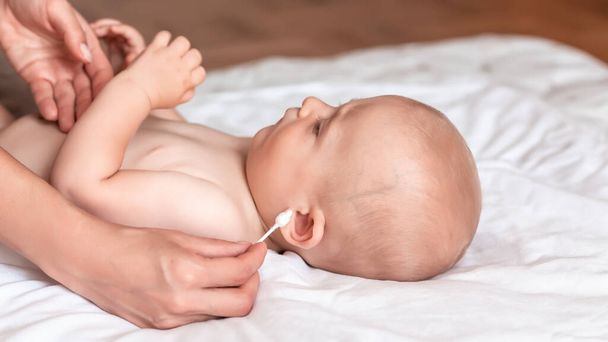 Mother cleaning her baby ears with cotton swab, hands cleaning ear of newborn baby, Newborn hygiene. concept cleaning wipe, pure, clean. - 写真・画像