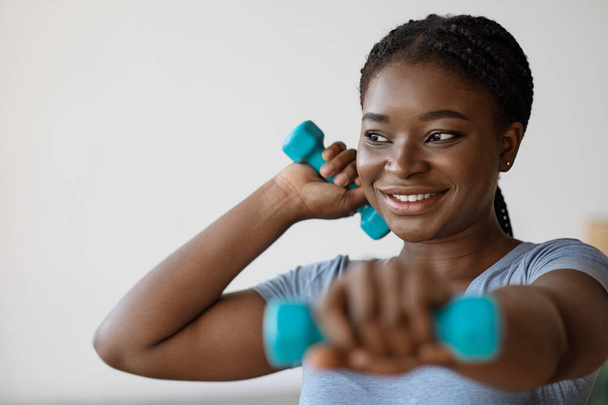 Vnitřní trénink. Usmívající se africká americká žena cvičení s činkami doma - Fotografie, Obrázek