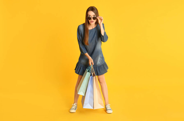 Beautiful young woman with paper shopping bags on yellow background - Photo, image