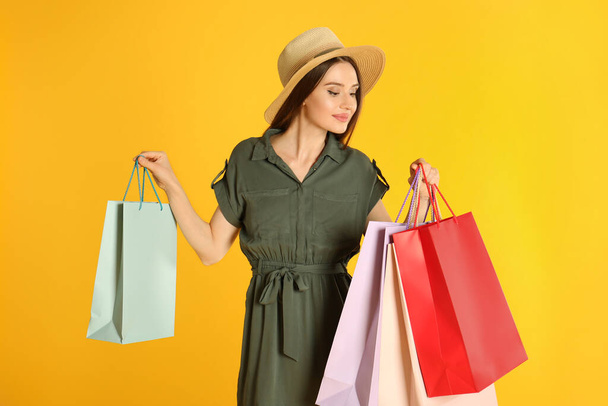 Beautiful young woman with paper shopping bags on yellow background - Фото, зображення