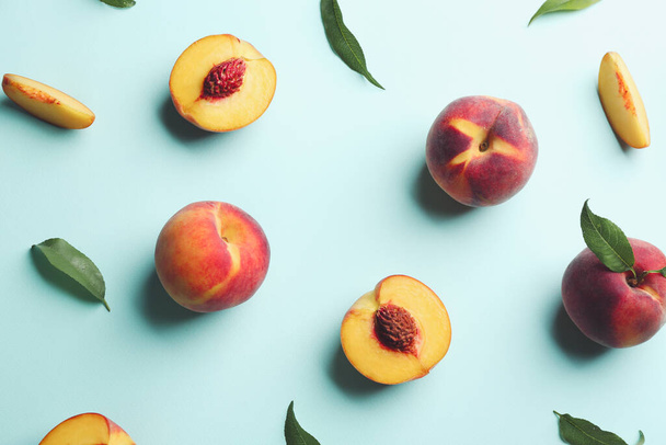 Fresh ripe peaches and green leaves on light blue background, flat lay - 写真・画像