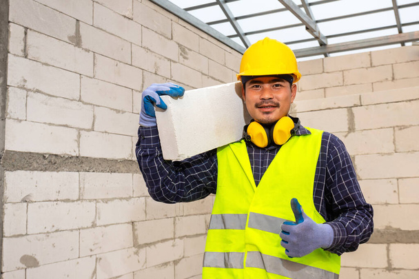 Worker reassure holds autoclaved aerated bricks in construction site, Concept proposes to use autoclaved aerated bricks in construction of houses. - Photo, Image
