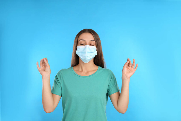 Woman in protective mask meditating on light blue background. Dealing with stress caused by COVID?19 pandemic - Φωτογραφία, εικόνα