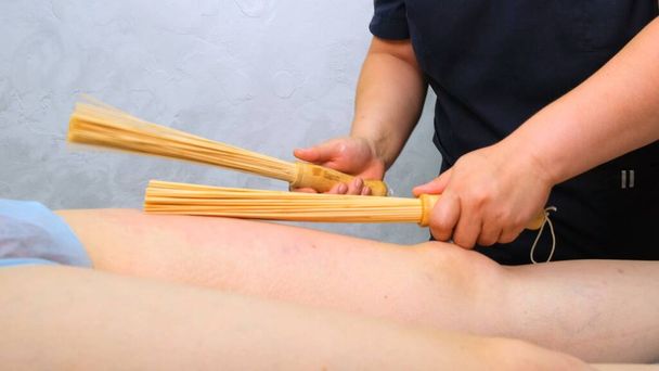 массажист делает антицеллюлитный массаж ног толстой женщине на массажном столе в спа-салоне с бамбуковой палкой. Спа процедуры. Здоровье и красота, питание - Фото, изображение