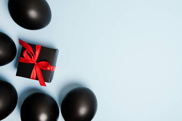 shiny black balloons and gift box with red ribbon on blue background , copy space - 写真・画像