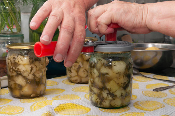 cooking canned vegetables. close up of hands are rolling up the lids with can sealing machine - Photo, Image