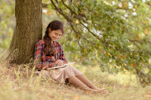 Dziewczyna czyta zabawną książkę pod drzewem w parku. - Zdjęcie, obraz