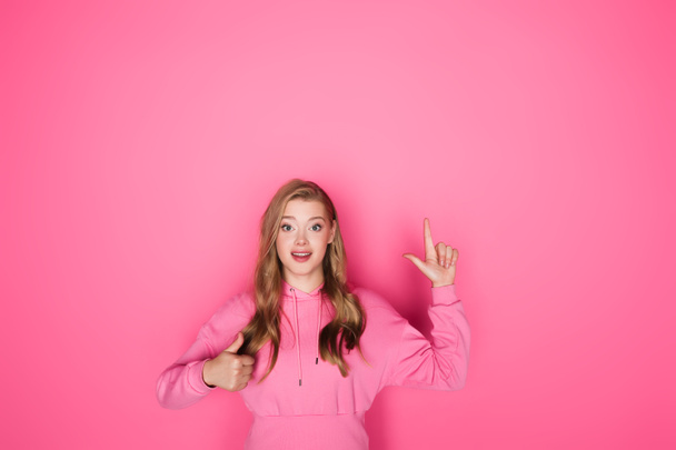 smiling beautiful woman pointing with finger and showing thumb up on pink background - 写真・画像