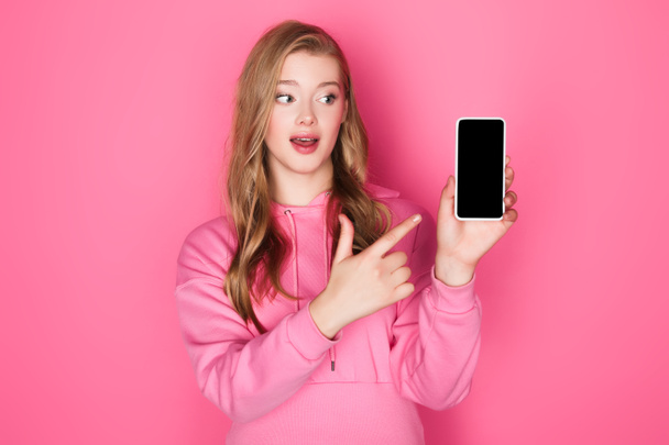 piękna kobieta wskazując na smartfona na różowym tle - Zdjęcie, obraz