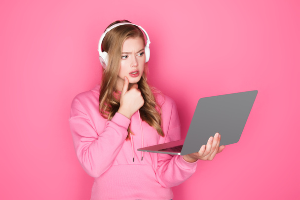 pensive beautiful woman in headphones with laptop on pink background - Photo, image