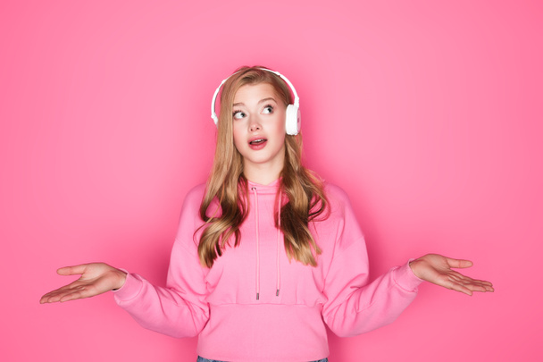 shocked beautiful woman listening music in headphones on pink background - Foto, afbeelding
