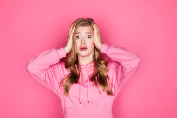 Schockiert schöne junge Frau in Kapuzenpulli mit Kopf auf rosa Hintergrund - Foto, Bild