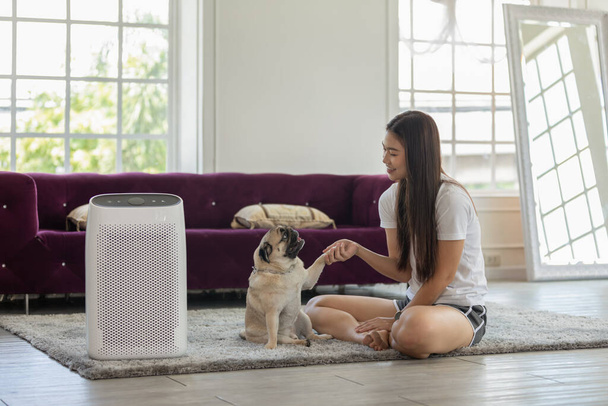 Woman playing with Dog Pug Breed and Air purifier in cozy white bed room for filter and cleaning removing dust PM2.5 HEPA in home,for fresh air and healthy life,Air Pollution Concept - Foto, Bild
